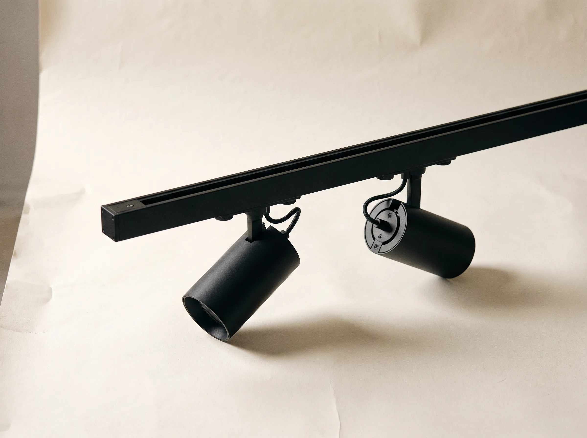Two adjustable cylinder spotlights mounted on a short section of matt black three-circuit lighting track.